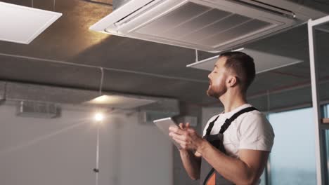 portrait-of-an-adult-man-in-a-work-uniform-installing-an-industrial-air-conditioner-and-configuring-software-in-a-modern-office