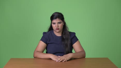 young overweight beautiful indian businesswoman against green background