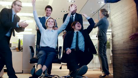 office chair race female and male business people ride chairs in the corporate building hallway. colleagues cheer and applaud. celebrate closing of the deal.