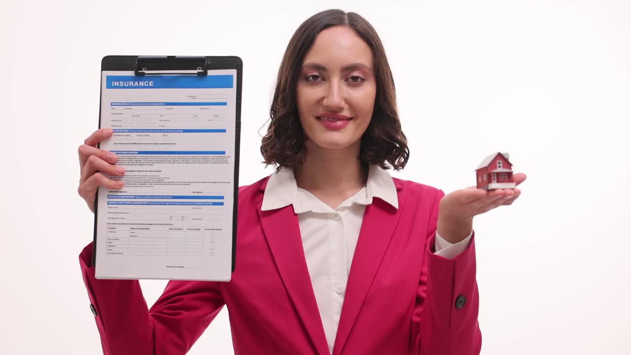 A woman in a pink blazer holding an insurance form and a miniature house model