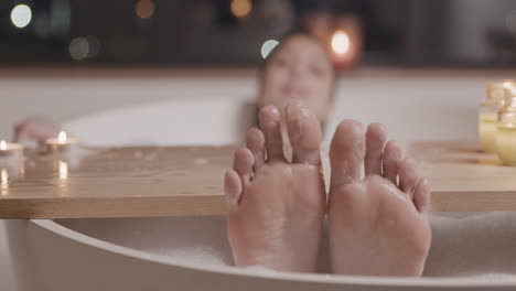 close up view of woman feet, she is taking a bath in the bathtub decorated by a wooden table with candles