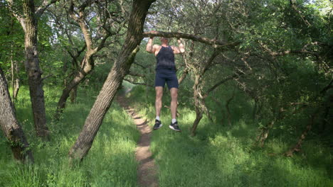 man doing pull-ups on a tree branch in a green forest