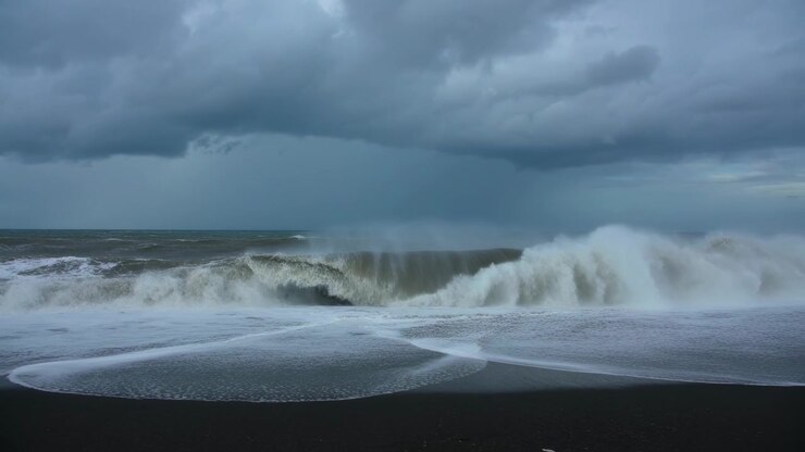 Vagues déferlantes poussées par la houle de tempête s'enroulant et se brisant sur une plage de sable noir, laissant des motifs de mousse.