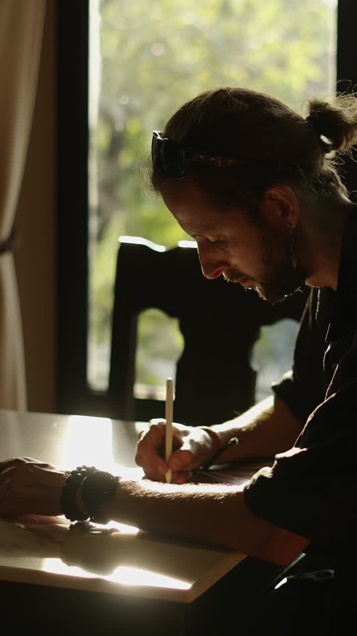 Uomo che disegna a un tavolo vicino a una finestra