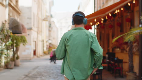 Vista-Trasera-De-Un-Turista-Feliz-Y-Relajado-Con-Auriculares-Inalámbricos-Escuchando-Música-Caminando-Por-Las-Calles-De-La-Ciudad