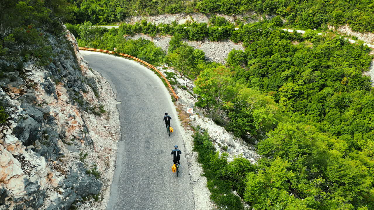 Aerial, drone view of people with yellow backpacks biking on the road in Bosnia and Herzegovina