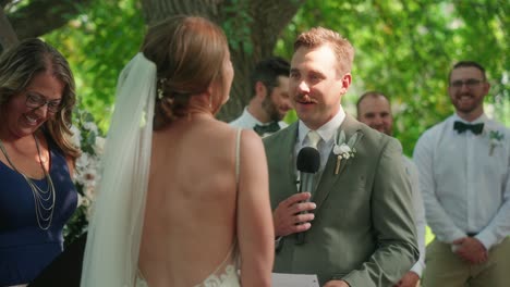 groom reads a joke in his vows, making everyone laugh during the outdoor ceremony