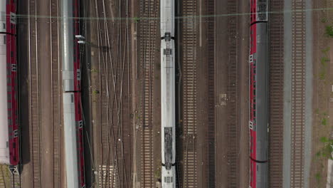 Aerial-Overhead-Top-Down-View-of-Passenger-Train-On-Multi-Track-Lane-with-Power-Lines-and-other-parked-Train-Wagons