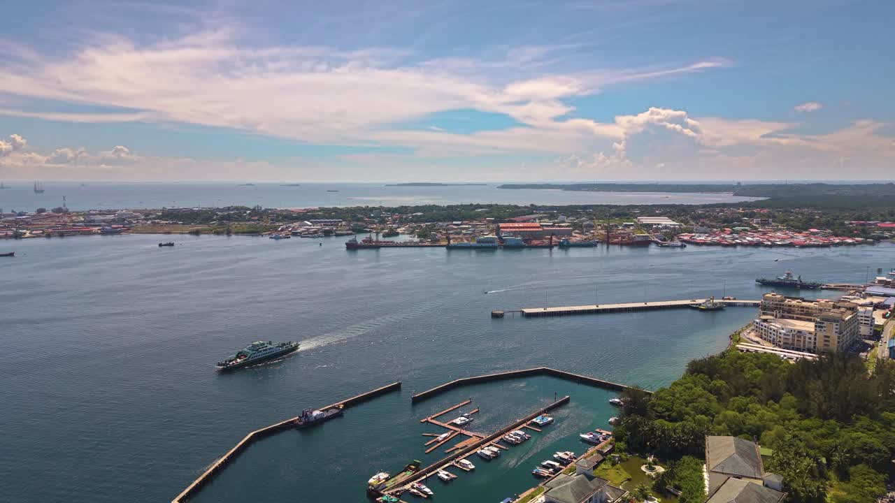 Aerial view of Labuan Island, Malaysia, showcasing a serene coastline, marina, and calm blue waters under a bright sky. Boats and buildings line the shore, revealing peaceful island life