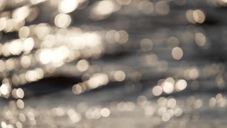 static slow motion shot of light shimmering off the water of the ocean, with waves and swells moving through, out of focus background