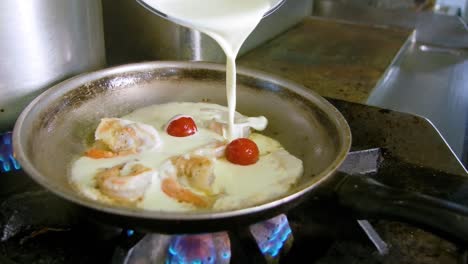 chef drizzles heavy cream into pan on gas stove with shrimp , omatoes and milky white suace