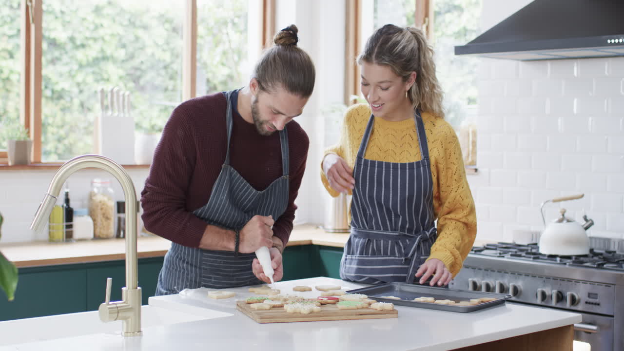 pareja feliz decorando galletas de navidad en la cocina en casa, en cámara lenta
