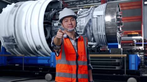 asian male engineer with safety helmet smiling and touching his chest then pointing at you while standing with airplane engine maintenance conducted, analytics checking the turbine