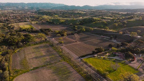 Aerial-Drone-Shot-of-Wine-Country-in-Santa-Ynez-California-at-Golden-Hour,-Vineyard-and-Fields-Below-with-Mountains-on-Horizon