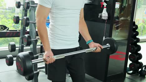 a young man in athletic wear selects a barbell from a rack and prepares to lift in a brightly lit, modern fitness center with large windows
