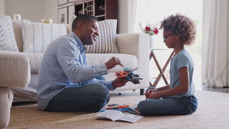 Niña-Preadolescente-Y-Abuelo-Sentados-En-El-Suelo-En-La-Sala-De-Estar-Construyendo-Un-Modelo-De-Robot,-Vista-Lateral