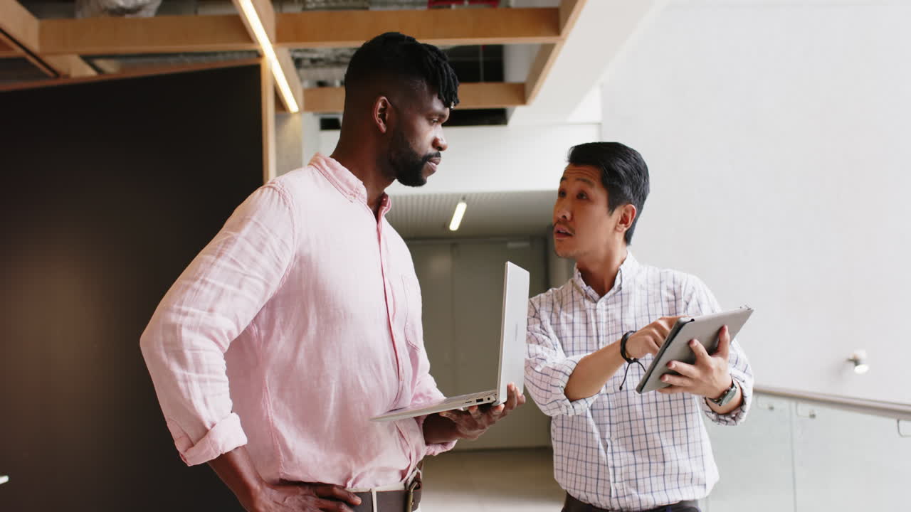Discussing project details, two men using laptop and tablet in office setting