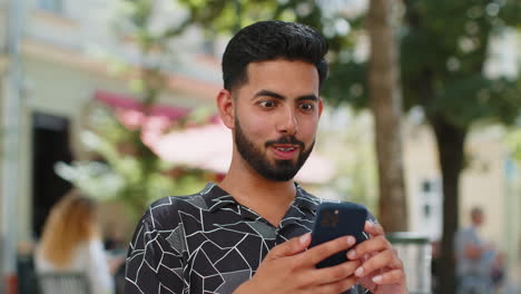 excited happy joyful winner indian man using smartphone celebrating win good message news outdoors