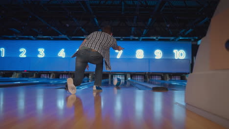 view from the back a man throws a ball and the camera follows him in a bowling club