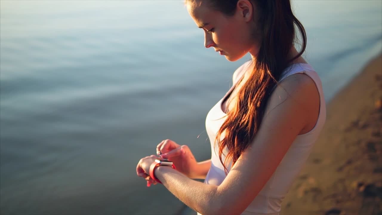 Woman Checking Smartwatch on Beach at Sunset