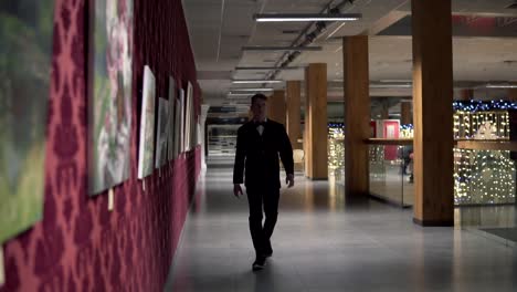 young blonde man in a black suit with bow-tie walking in the art gallery. slow motion