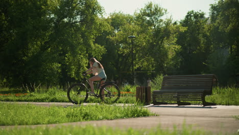 cyclist mounts bicycle near vibrant garden, preparing for ride surrounded colorful flower beds under warm sunlight, background includes trees, people strolling, and a wooden bench