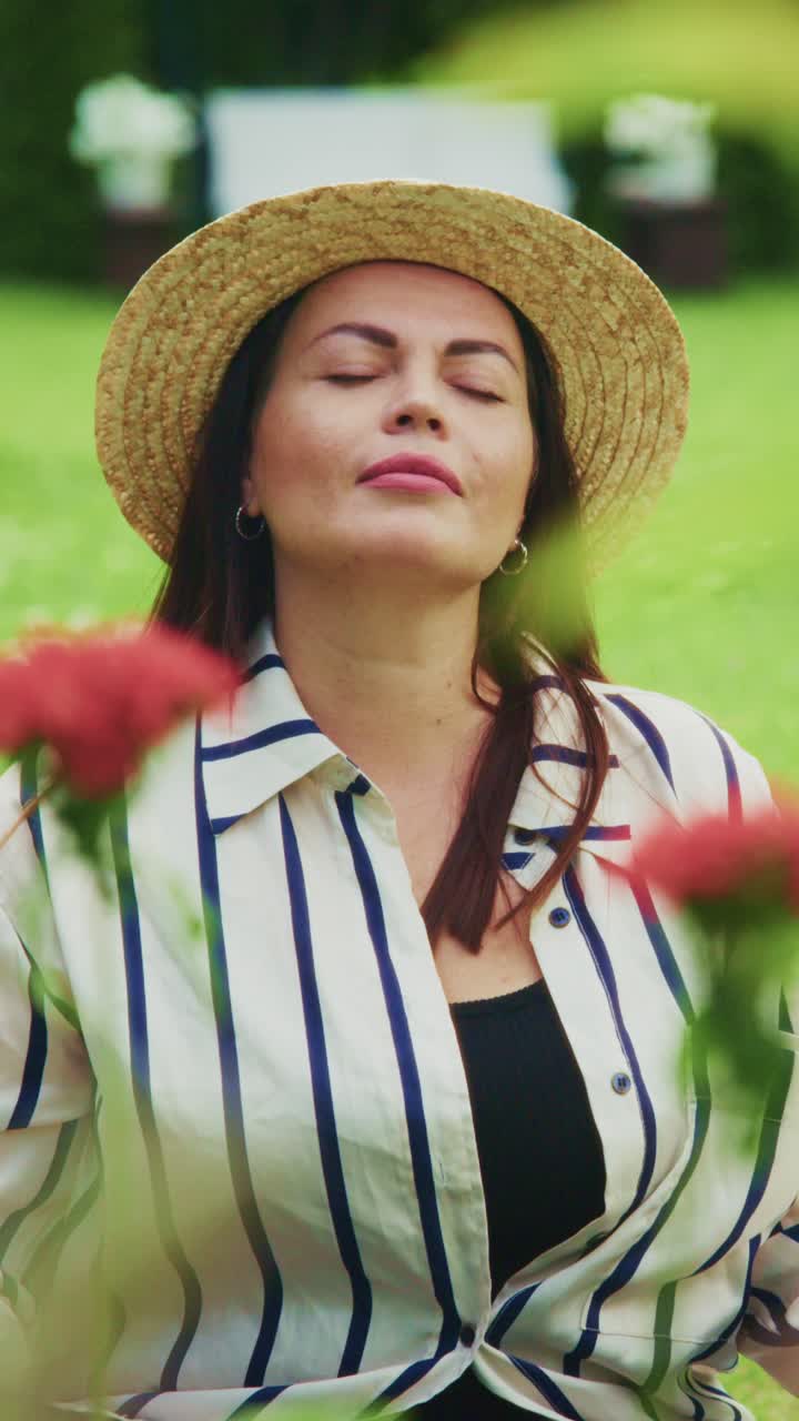 A Woman in a Straw Hat Closely Connecting with Nature while Savoring the Peaceful Surroundings Amidst Colorful Flowers in a Lush Green Field