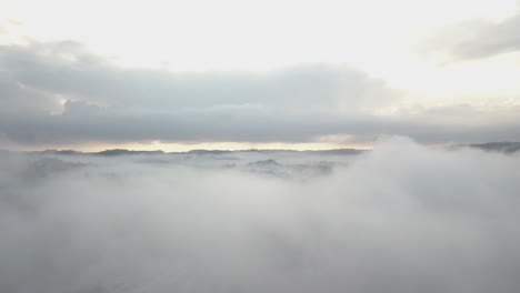 Aerial,-drone-shot,-over-thick-fog,-in-middle-of-hills-and-forest,-on-a-foggy,-autumn-day,-in-Birkeland,-Aust-Agder,-South-Norway