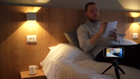 joven blogger masculino, grabando video con su teléfono inteligente, gestando