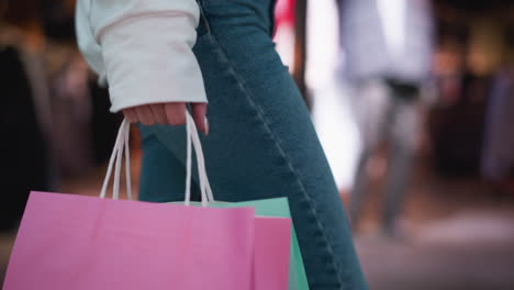 bolsa de compras rosada sostenida en la mano pulida con bolsa de color menta ligeramente visible, puesta contra el vibrante fondo del centro comercial con exhibición de maniquíes, reflejos borrosos de vidrio y luces