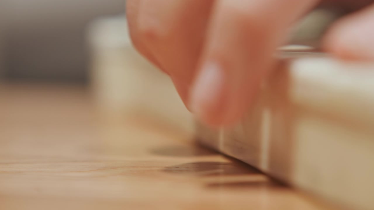 Close up of hand opening and closing latch on off white plastic box with faint floral pattern resting steadily across smooth wooden surface. Hand movement is deliberate as it engages metal