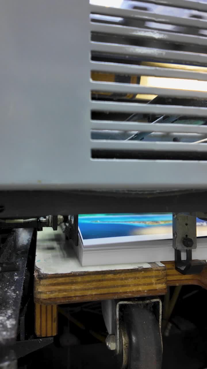 Uma máquina de impressão opera em alta velocidade, com garras liberando papel por trás de uma grade de segurança. O processo é eficiente e destaca a mecânica intrincada envolvida no manuseio do papel