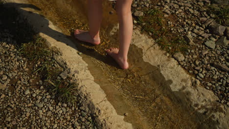 little girl feet walking alone in forest stream and enjoys nature. active child explores environment. recreation and awesome adventures with kid on warm summer day