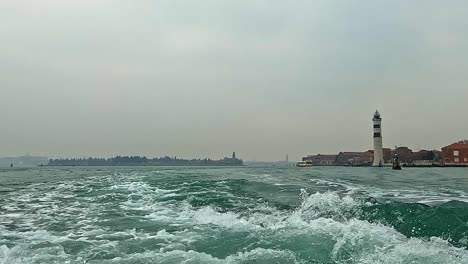 ángulo-Bajo-De-La-Superficie-Del-Agua-Pov-Del-Faro-De-Murano-En-La-Laguna-De-Venecia-Visto-Desde-El-Ferry,-Italia