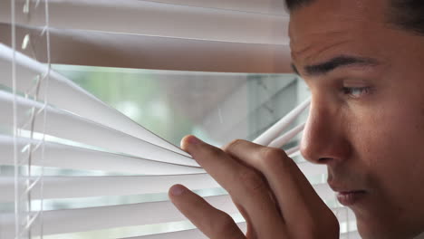 Young-man-opens-the-blind-peeking-through-Venetian-blinds-from-an-indoor-office