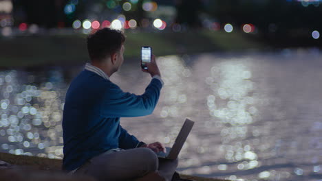 young man using laptop and photographing city in the evening