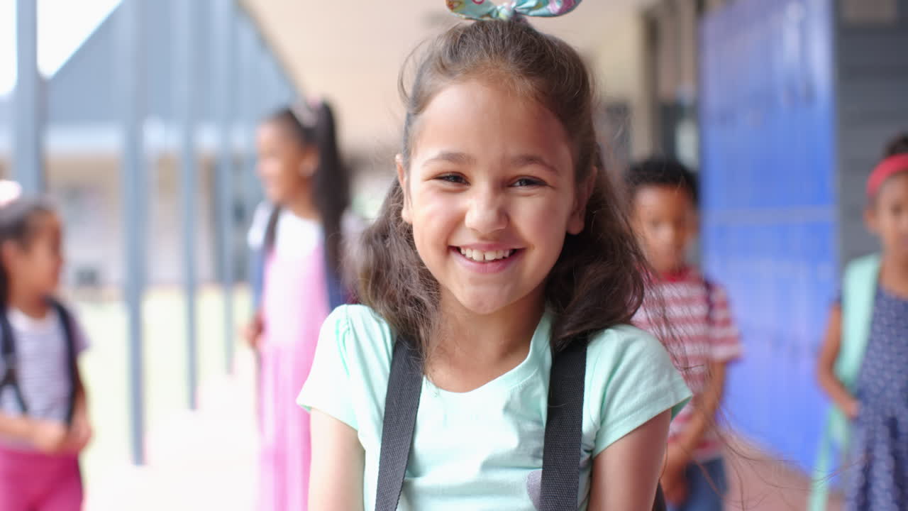 Smiling girl with backpack standing in school hallway with classmates in background