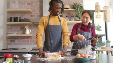 happy diverse couple in aprons using tablet and baking in kitchen, slow motion