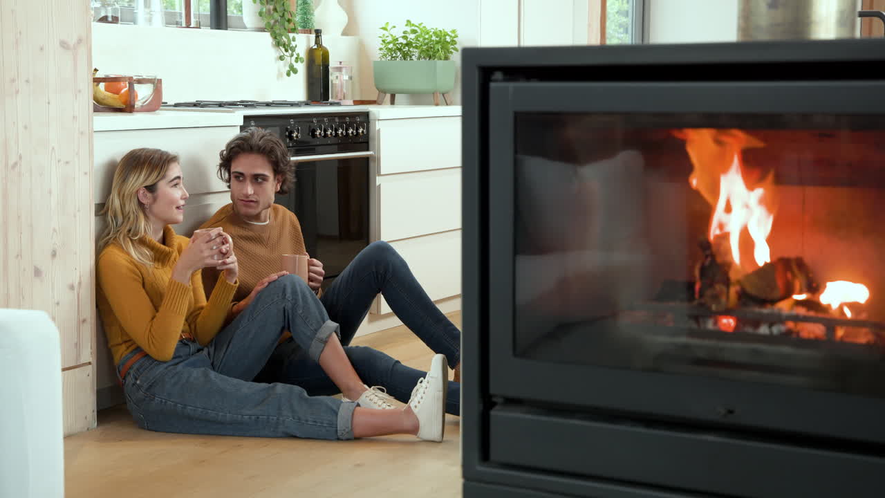 Couple enjoying hot drinks by cozy fireplace in modern kitchen