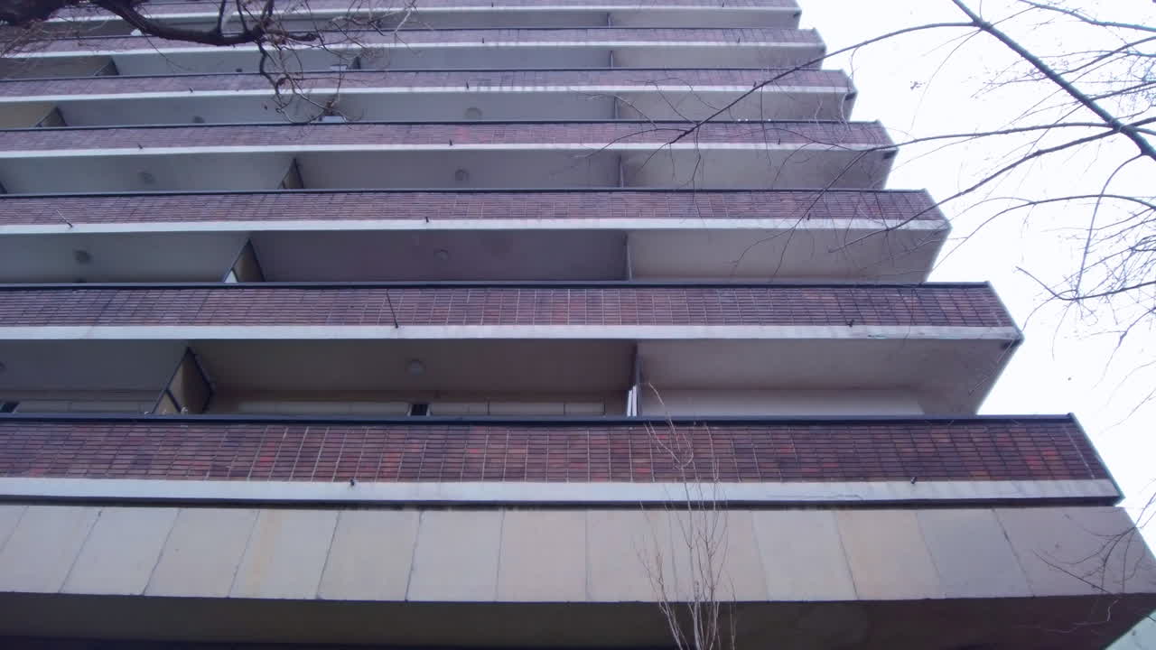 Movimiento cinematográfico de paneo ascendente que muestra los patrones horizontales repetitivos de los balcones de un gran bloque de apartamentos residenciales. Claro detalle arquitectónico de vivienda social urbana en un distrito de la ciudad.