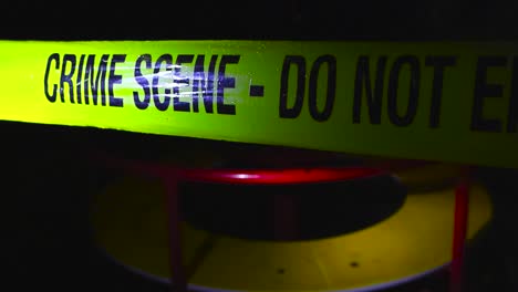 close up or closeup footage of a yellow colored crime scene do not enter police caution tape ribbon pulled in front of a merry go round spinning in a dark and rainy night, raindropds on the tape