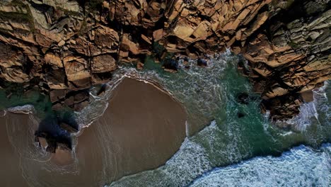 aerial view over a cornish beach with ocean waves rolling against the rocky cliff face