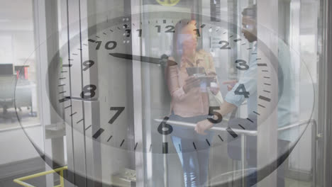 Animation-of-ticking-clock-against-diverse-man-and-woman-discussing-in-elevator-at-office