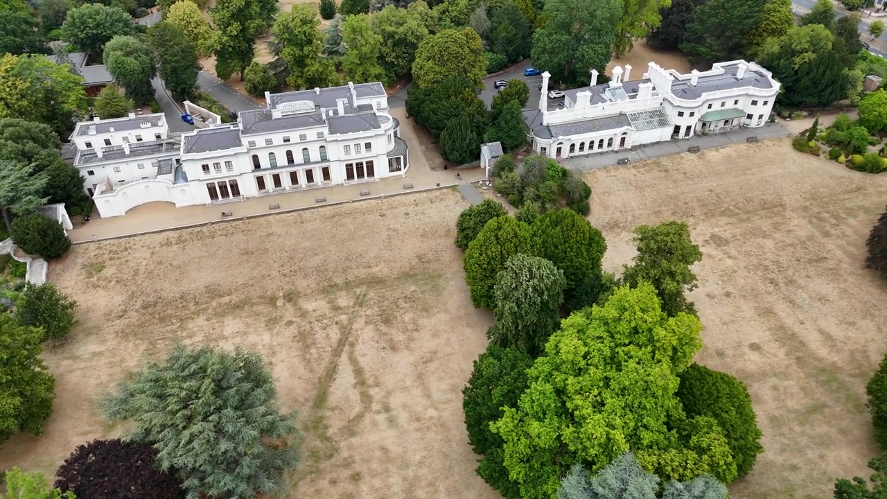 Coppia di ville in stucco bianco si affacciano su un parco ingiallito dalla siccità con cedri e alberi maturi intorno.