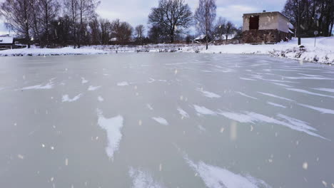 frozen lake water in city park during snowfall in aerial low altitude slow flying shot