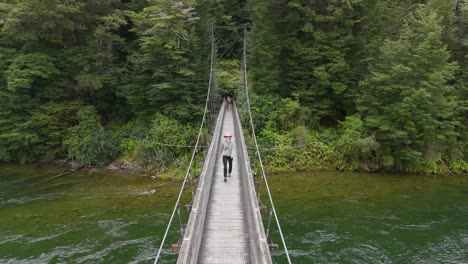 Toma-Aérea-De-Una-Turista-Caminando-Sobre-El-Puente-Del-Arco-Iris-Al-Comienzo-De-La-Pista-Kepler-En-Nueva-Zelanda