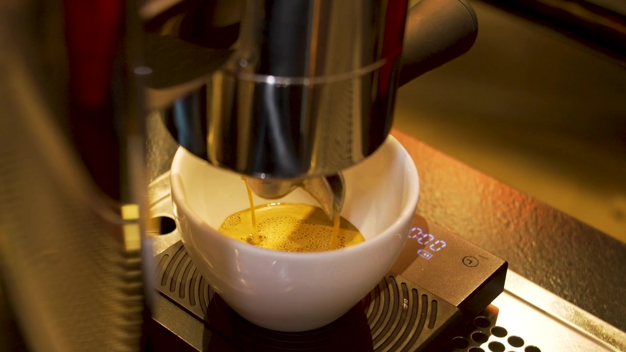 Caffè espresso che si versa in una tazza di ceramica bianca oversize al bancone di una caffetteria specializzata.