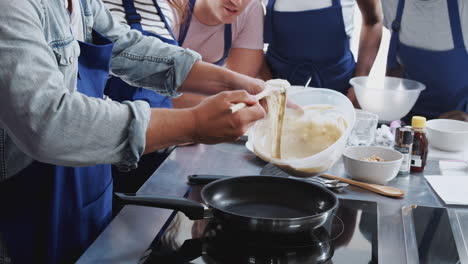 primer plano de un profesor masculino añadiendo mezcla a la sartén en la clase de cocina