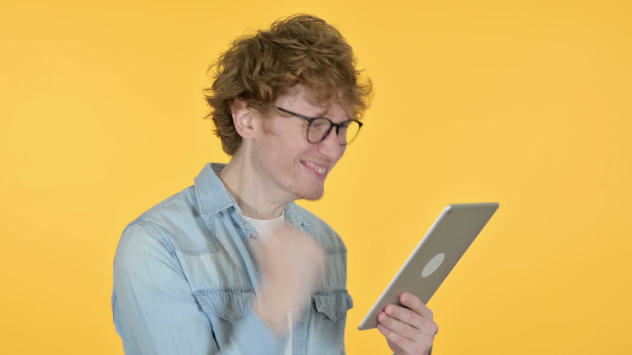 Redhead Young Man Celebrating on Tablet, Yellow Background