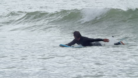 sportive man in wetsuit with artificial leg lying on surfboard and swimming in the ocean 7